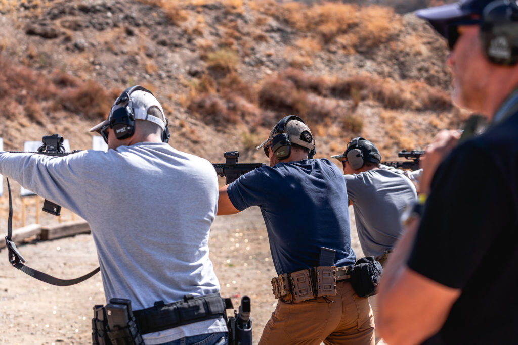 People practicing shooting at a firing range with ear protection and firearms.